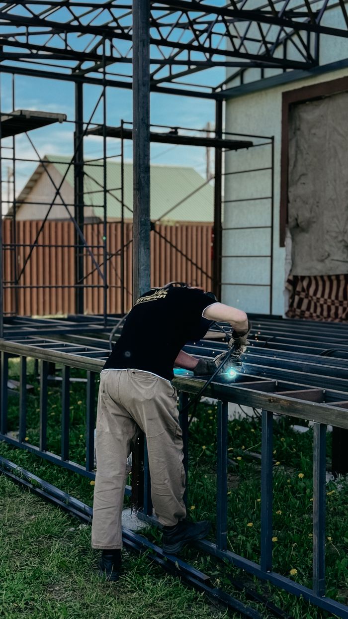 Quien Somos A skilled welder working on a metal structure in an outdoor setting, showcasing construction expertise.