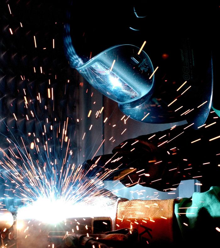 Quien Somos A focused welder works with metal in an industrial setting, creating vibrant sparks.